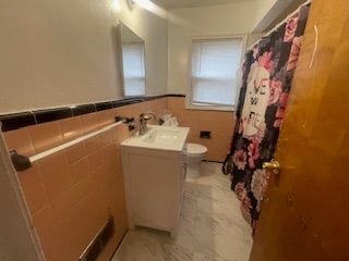 bathroom with tile walls, curtained shower, vanity, a wainscoted wall, and toilet