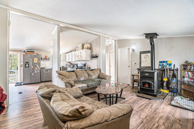living area featuring vaulted ceiling, ornamental molding, light wood-style flooring, and a wood stove