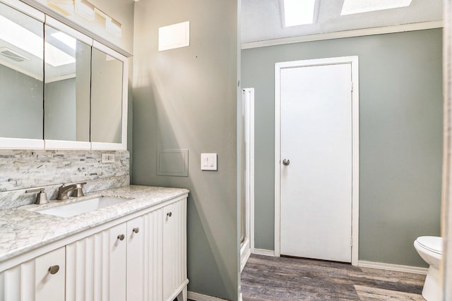 bathroom with vanity, toilet, baseboards, wood finished floors, and backsplash