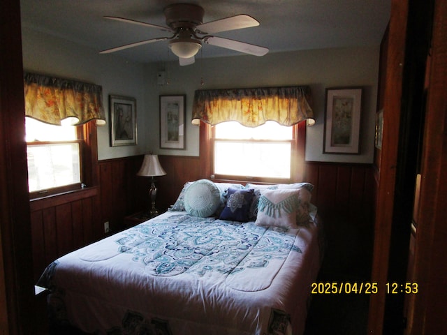 975 N Huron, East Tawas, MI 48730 - bedroom featuring wooden walls, a wainscoted wall, a ceiling fan, and multiple windows