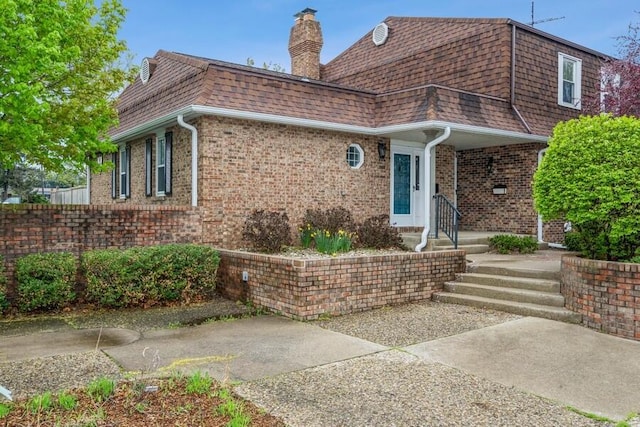 view of front of home with a shingled roof, a chimney, mansard roof, and brick siding
