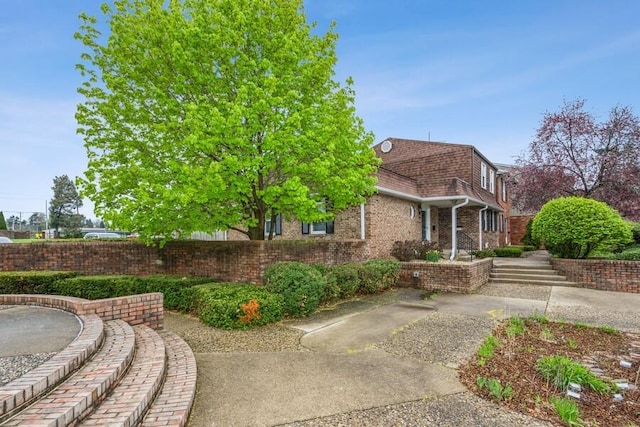view of property exterior with fence, mansard roof, roof with shingles, and brick siding