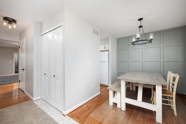 568 Foxboro Sq Unit 59, Brighton, MI 48116 - unfurnished dining area featuring visible vents, wood-type flooring, a decorative wall, baseboards, and a notable chandelier