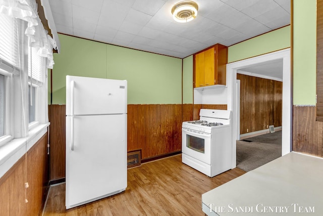 kitchen with wood walls, a wainscoted wall, white appliances, and light wood finished floors