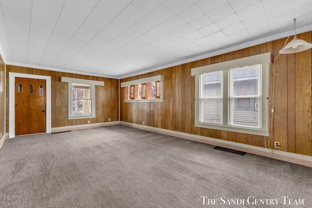 unfurnished living room with crown molding, carpet flooring, wooden walls, and visible vents