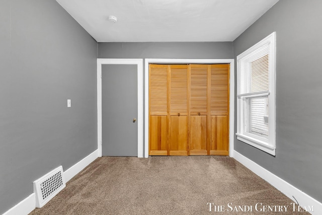 unfurnished bedroom featuring carpet floors, baseboards, a closet, and visible vents