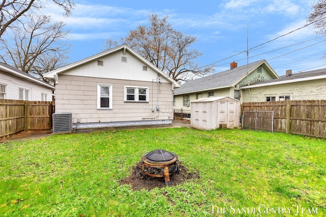 rear view of house featuring a lawn, central AC unit, a shed, a fenced backyard, and an outdoor fire pit