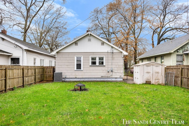 back of property featuring a storage shed, a yard, a fire pit, and a fenced backyard