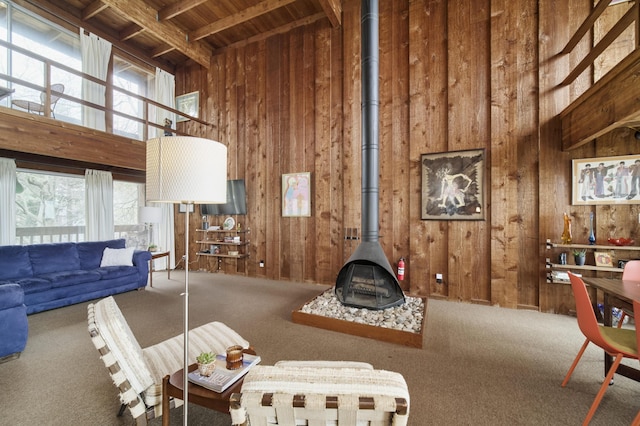 carpeted living room with a wood stove, a high ceiling, wooden walls, and wooden ceiling