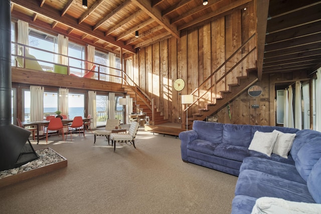 carpeted living room with a wood stove, stairs, a healthy amount of sunlight, and wooden ceiling