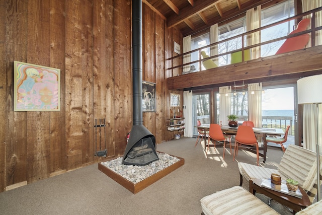 carpeted living area with a high ceiling, wood walls, wooden ceiling, and a wood stove