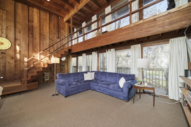 living area featuring carpet flooring, high vaulted ceiling, wood walls, and stairs