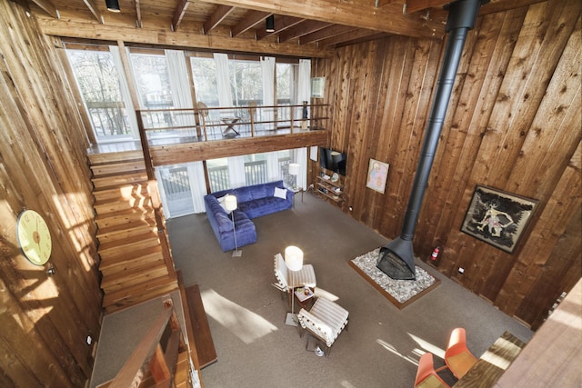 living room featuring a wood stove, carpet, wooden walls, and beamed ceiling