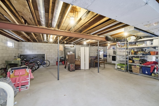 unfinished basement with freestanding refrigerator and concrete block wall