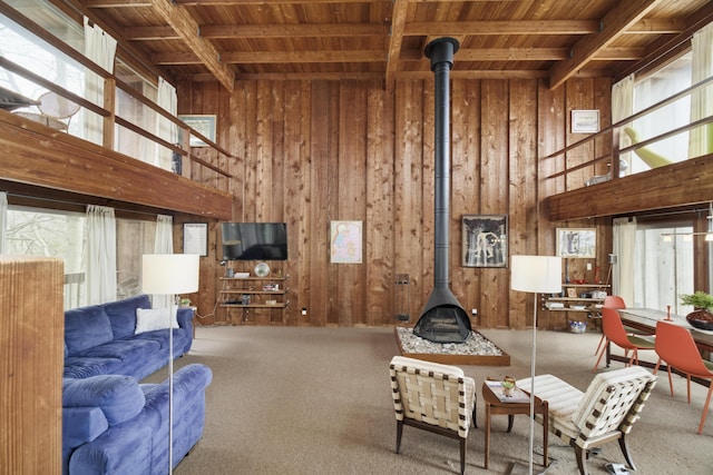 carpeted living area with wood ceiling, a wood stove, beam ceiling, wooden walls, and a wealth of natural light