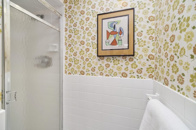 bathroom with a wainscoted wall, a shower stall, and wallpapered walls