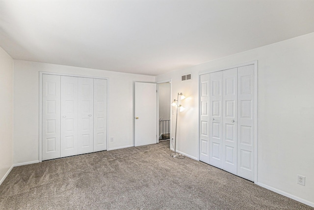 unfurnished bedroom featuring two closets, carpet floors, and baseboards