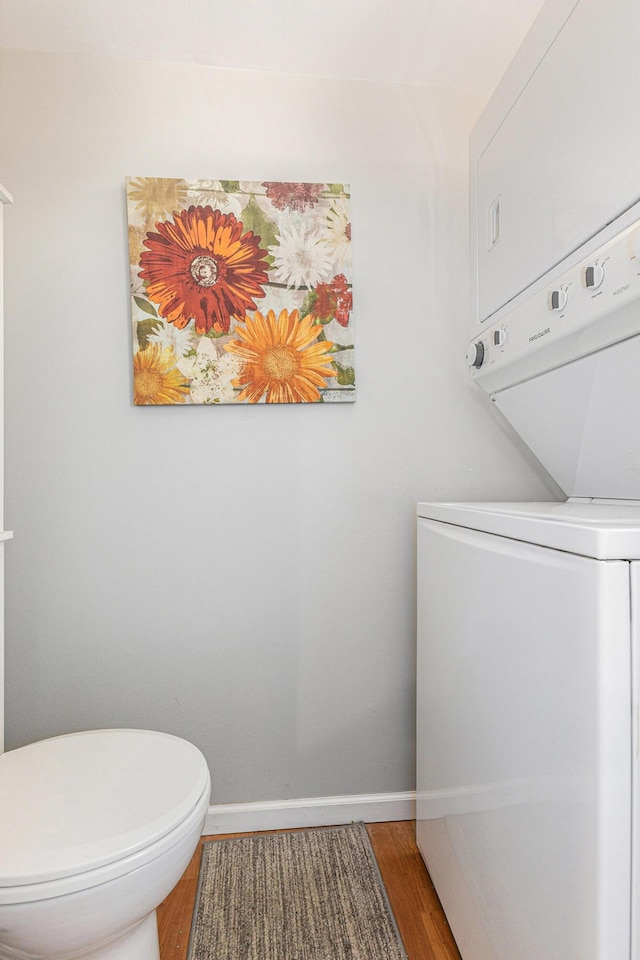bathroom with stacked washing machine and dryer, baseboards, wood finished floors, and toilet