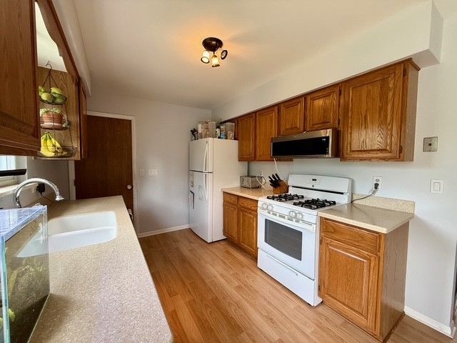 kitchen with a sink, white appliances, light countertops, brown cabinetry, and light wood-type flooring