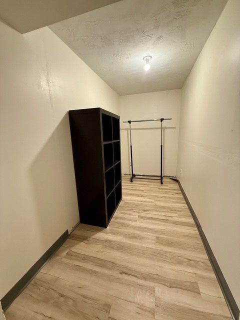 corridor with a textured ceiling, baseboards, and light wood-style floors