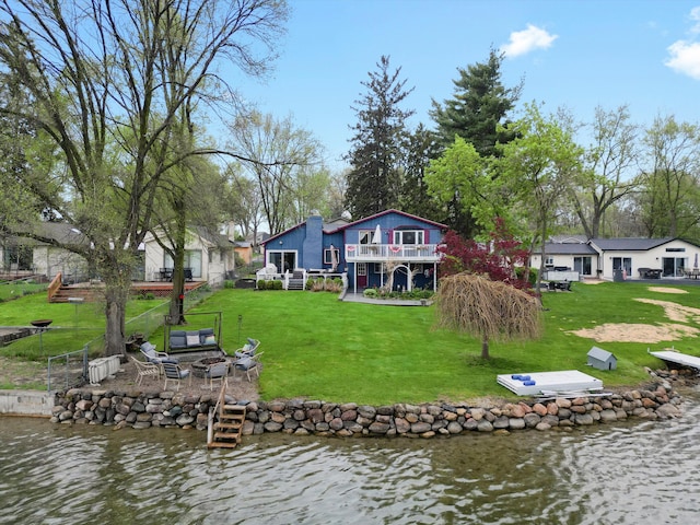 back of house featuring a deck with water view, a yard, and an outdoor fire pit