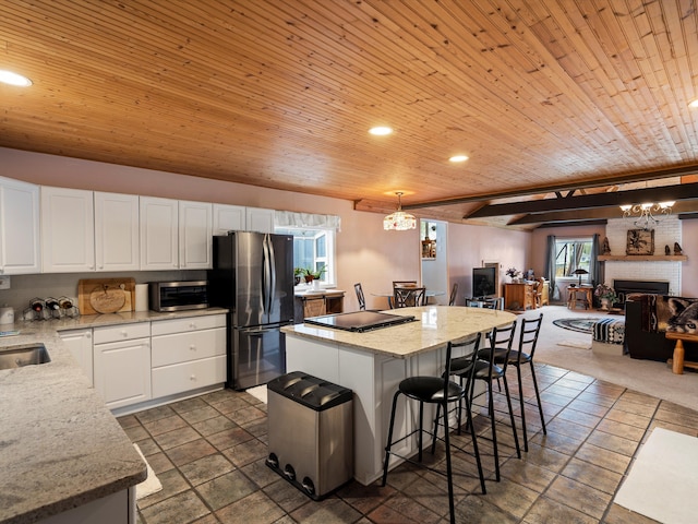 kitchen with freestanding refrigerator, a kitchen island, open floor plan, white cabinets, and a sink