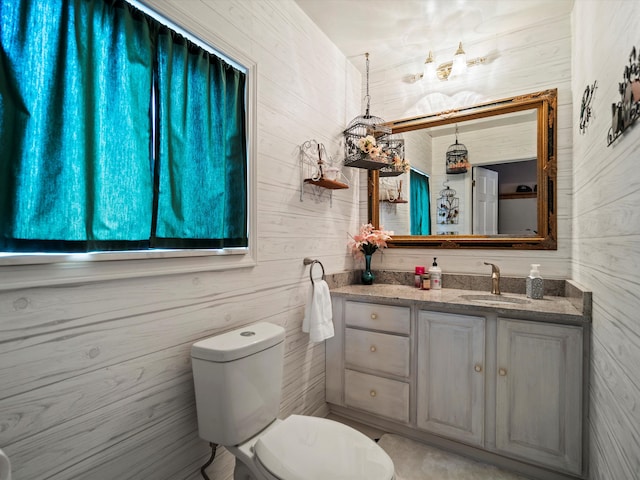 bathroom featuring toilet, wood walls, and vanity