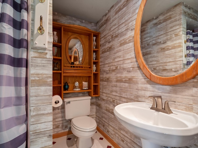bathroom with wooden walls, toilet, a shower with curtain, and a sink