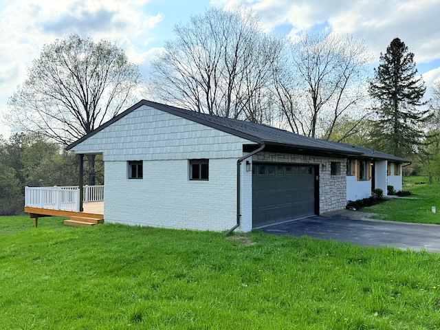 view of side of home with an attached garage, brick siding, aphalt driveway, a deck, and a yard