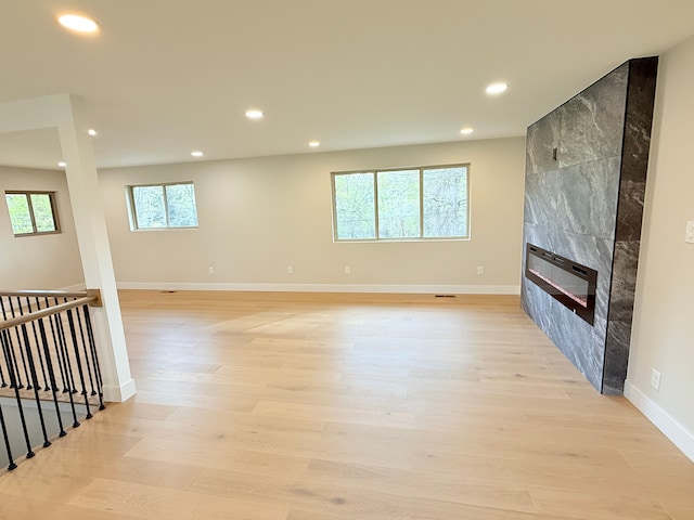 unfurnished living room with recessed lighting, baseboards, a tile fireplace, and light wood-style floors