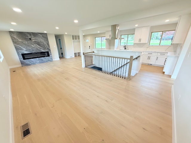 unfurnished living room featuring a sink, recessed lighting, light wood-style flooring, and visible vents