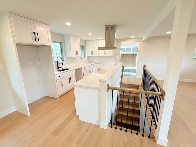kitchen with a sink, light wood-type flooring, island range hood, and light stone counters