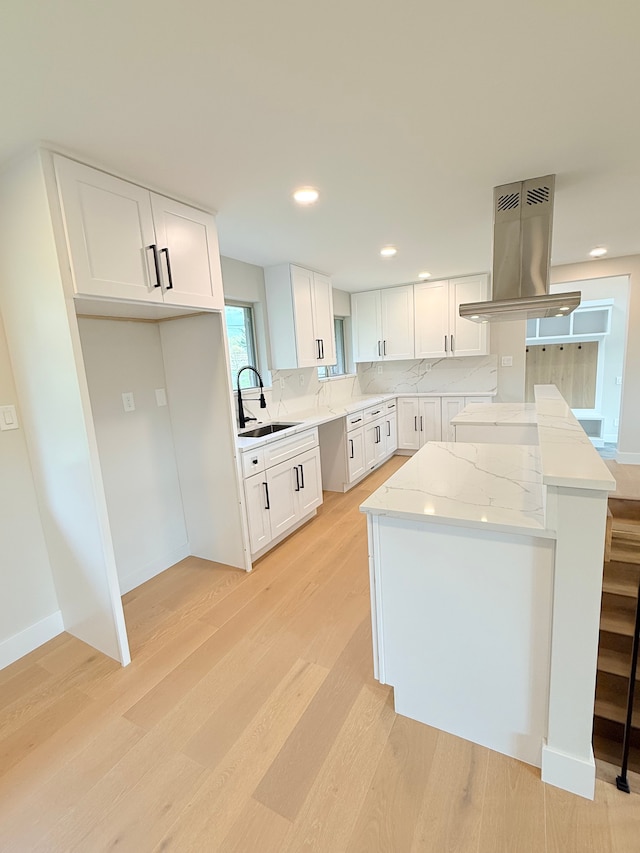 kitchen featuring backsplash, island exhaust hood, a sink, white cabinets, and light wood-style floors