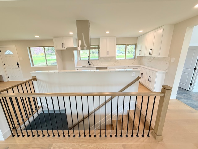 kitchen featuring island exhaust hood, white cabinetry, plenty of natural light, and backsplash