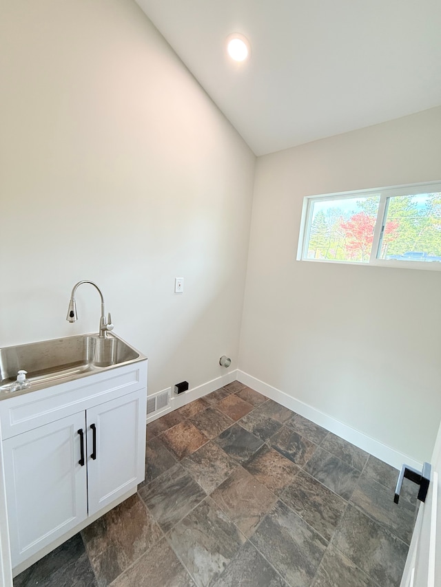 laundry area featuring visible vents, stone tile floors, baseboards, a sink, and cabinet space