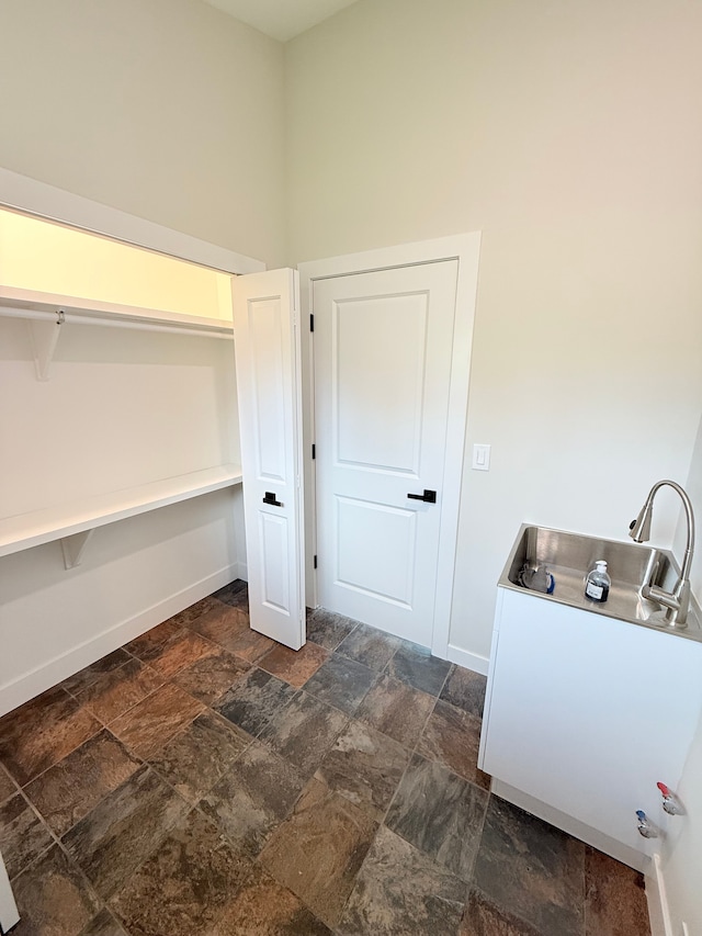 clothes washing area with baseboards and stone finish floor