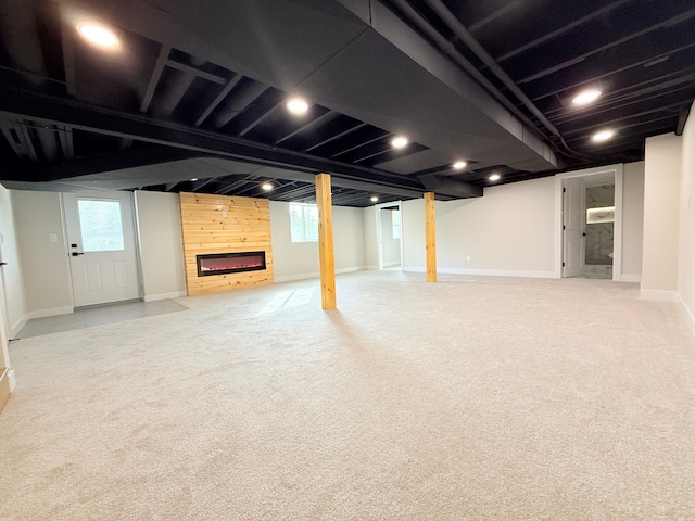 below grade area featuring light colored carpet, baseboards, and a large fireplace