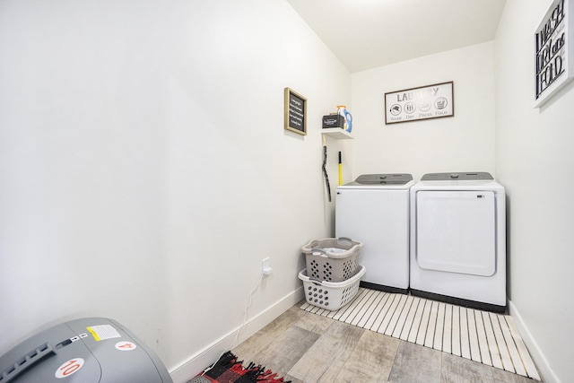 clothes washing area with washing machine and clothes dryer, laundry area, baseboards, and wood finished floors
