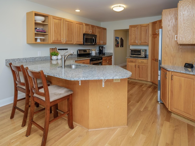 kitchen with a peninsula, a kitchen bar, a sink, light wood finished floors, and stainless steel appliances