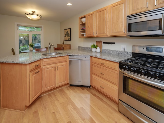 kitchen featuring light stone countertops, appliances with stainless steel finishes, a sink, a peninsula, and light wood-type flooring