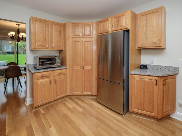 kitchen featuring light stone countertops, a notable chandelier, light wood-style floors, freestanding refrigerator, and a toaster