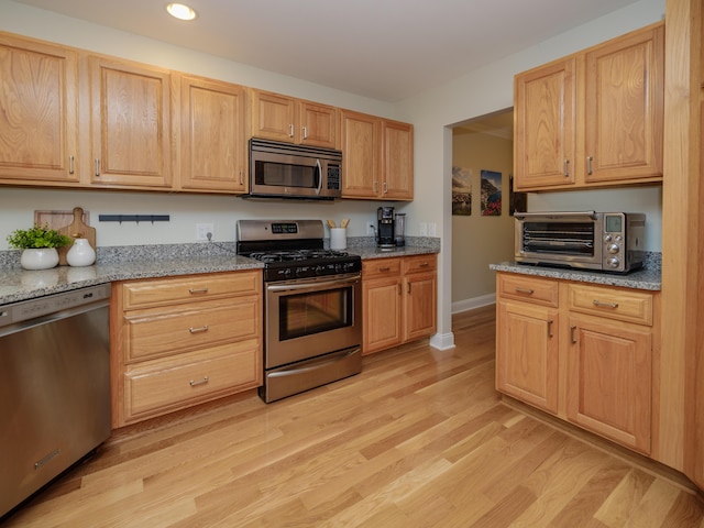 kitchen featuring appliances with stainless steel finishes, light stone counters, light wood finished floors, recessed lighting, and a toaster