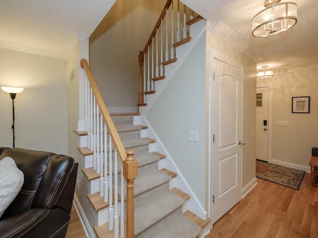 staircase with crown molding, baseboards, wood finished floors, and a notable chandelier