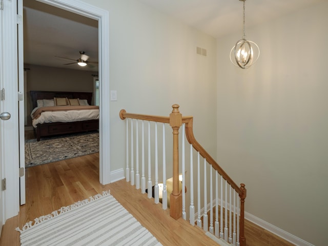 corridor featuring visible vents, an upstairs landing, wood finished floors, baseboards, and a notable chandelier