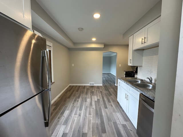 kitchen featuring white cabinets, a sink, light wood-style flooring, stainless steel appliances, and decorative backsplash