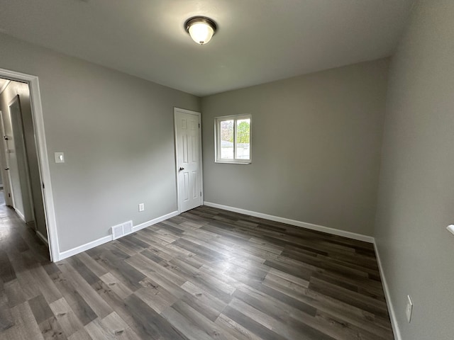spare room featuring baseboards, dark wood-style flooring, and visible vents