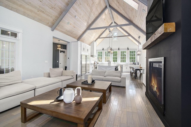 living room with beam ceiling, high vaulted ceiling, hardwood / wood-style floors, wooden ceiling, and a lit fireplace