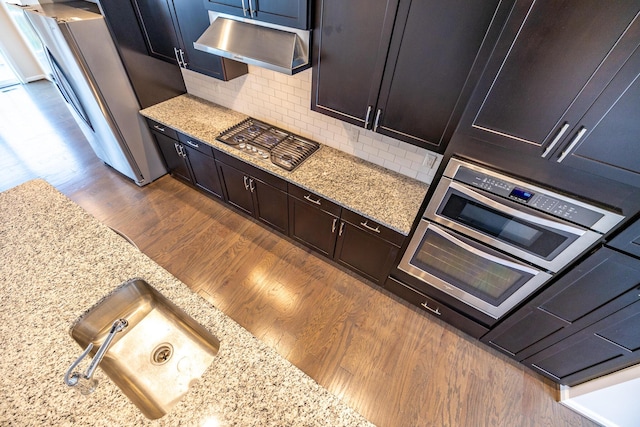 kitchen with dark wood-style flooring, tasteful backsplash, light stone counters, under cabinet range hood, and stainless steel appliances