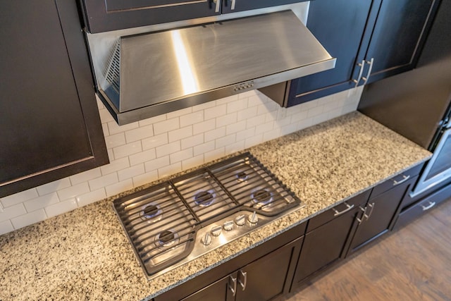 room details featuring decorative backsplash, stainless steel gas cooktop, light stone countertops, dark wood-style floors, and under cabinet range hood