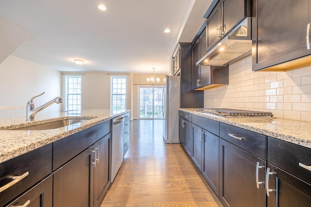 kitchen featuring an inviting chandelier, light stone counters, a sink, light wood-style flooring, and appliances with stainless steel finishes
